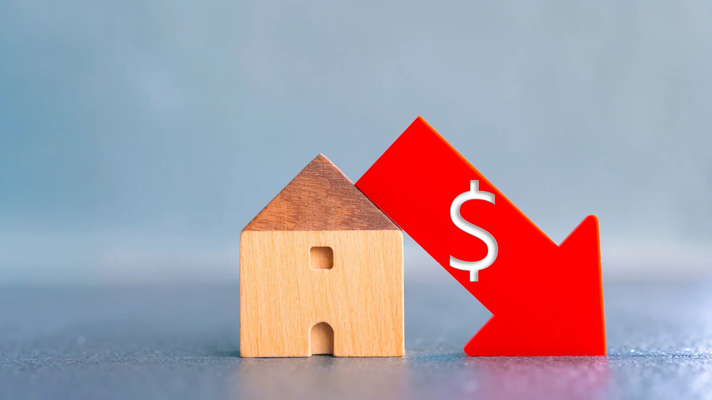 Wooden house beside a red downward arrow with a dollar sign.