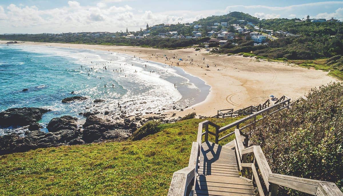 Wooden stairs lead to a populated beach and ocean.