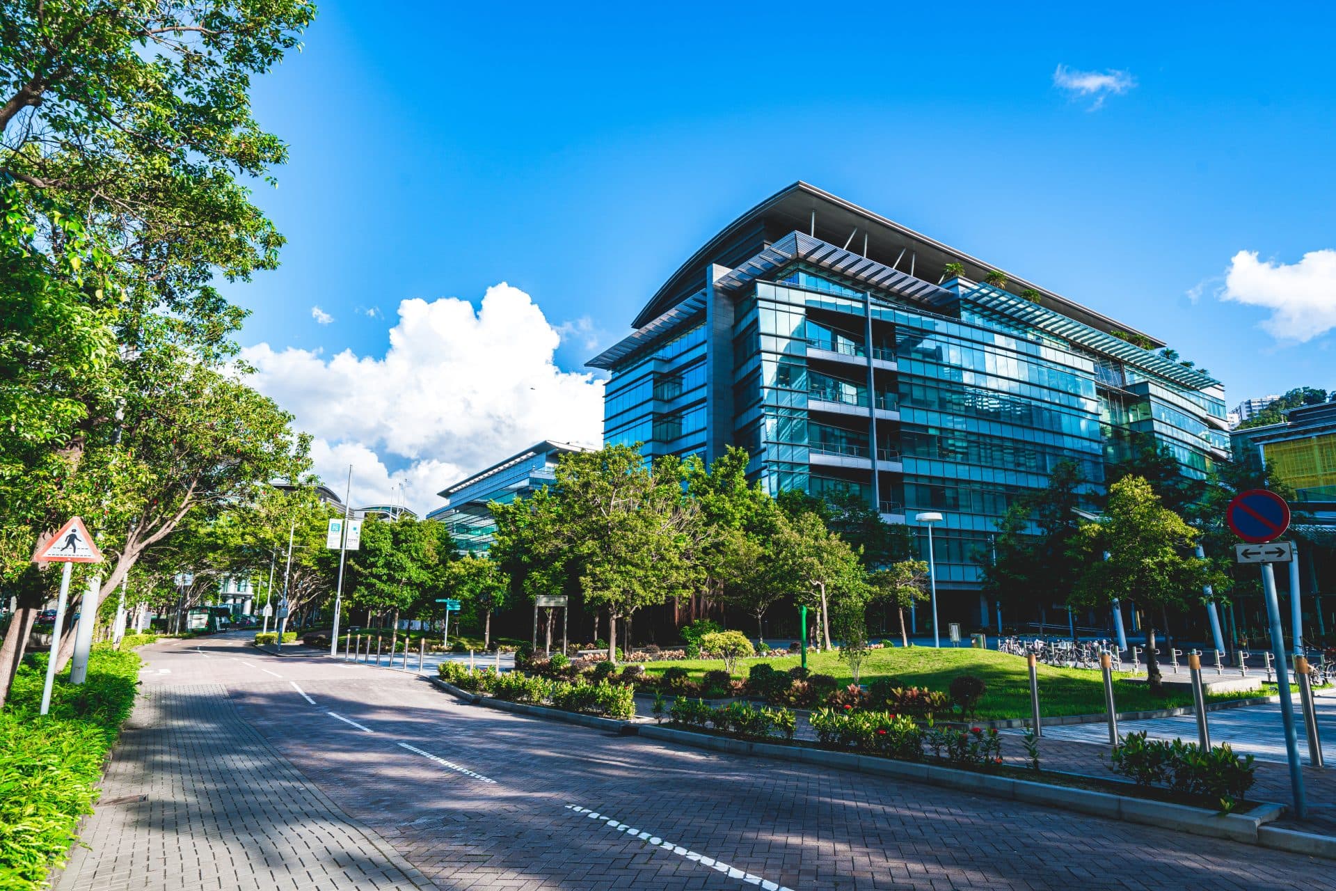Modern glass buildings by a tree-lined street.