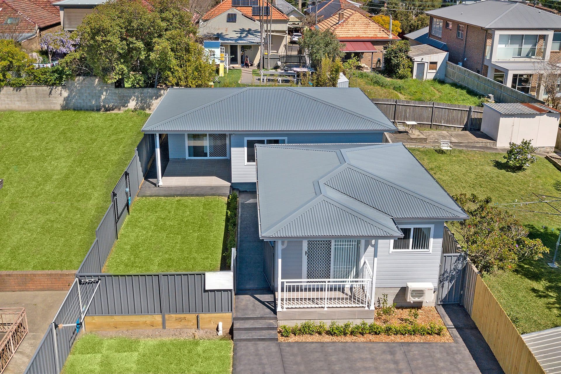 Two modern grey houses with green lawns.