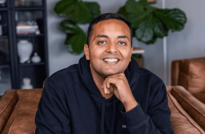 Man in dark hoodie resting chin on hand, smiling.