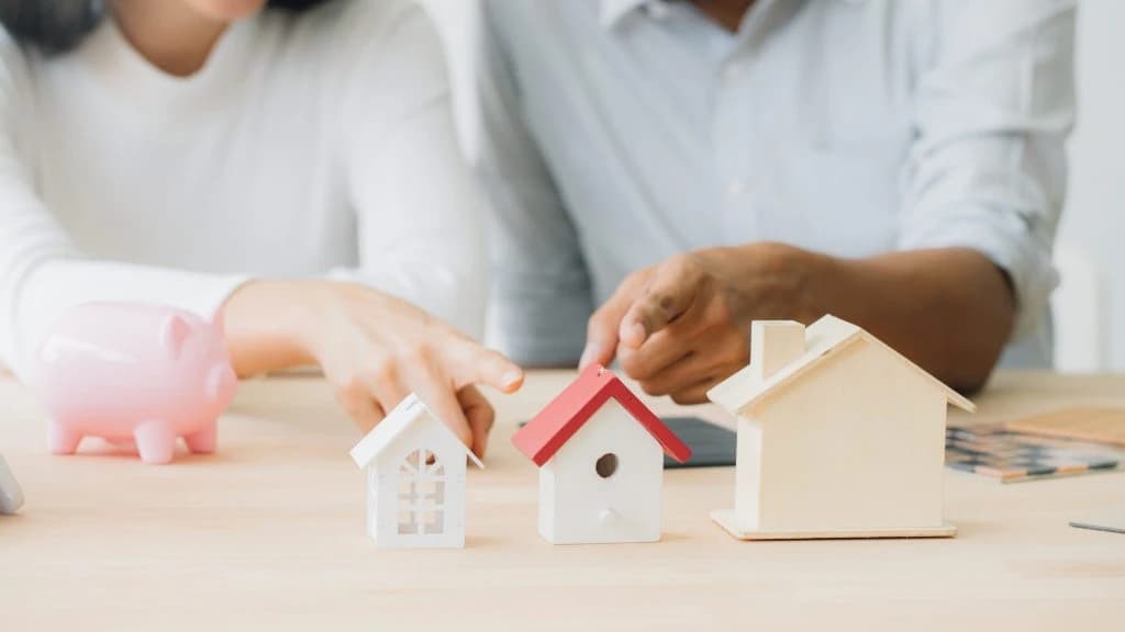Miniature houses, piggy bank, and hands pointing.