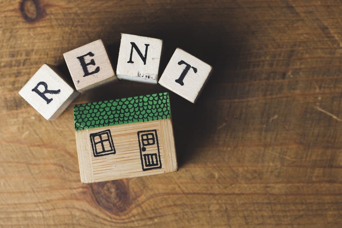 Wooden blocks spelling RENT with a toy house