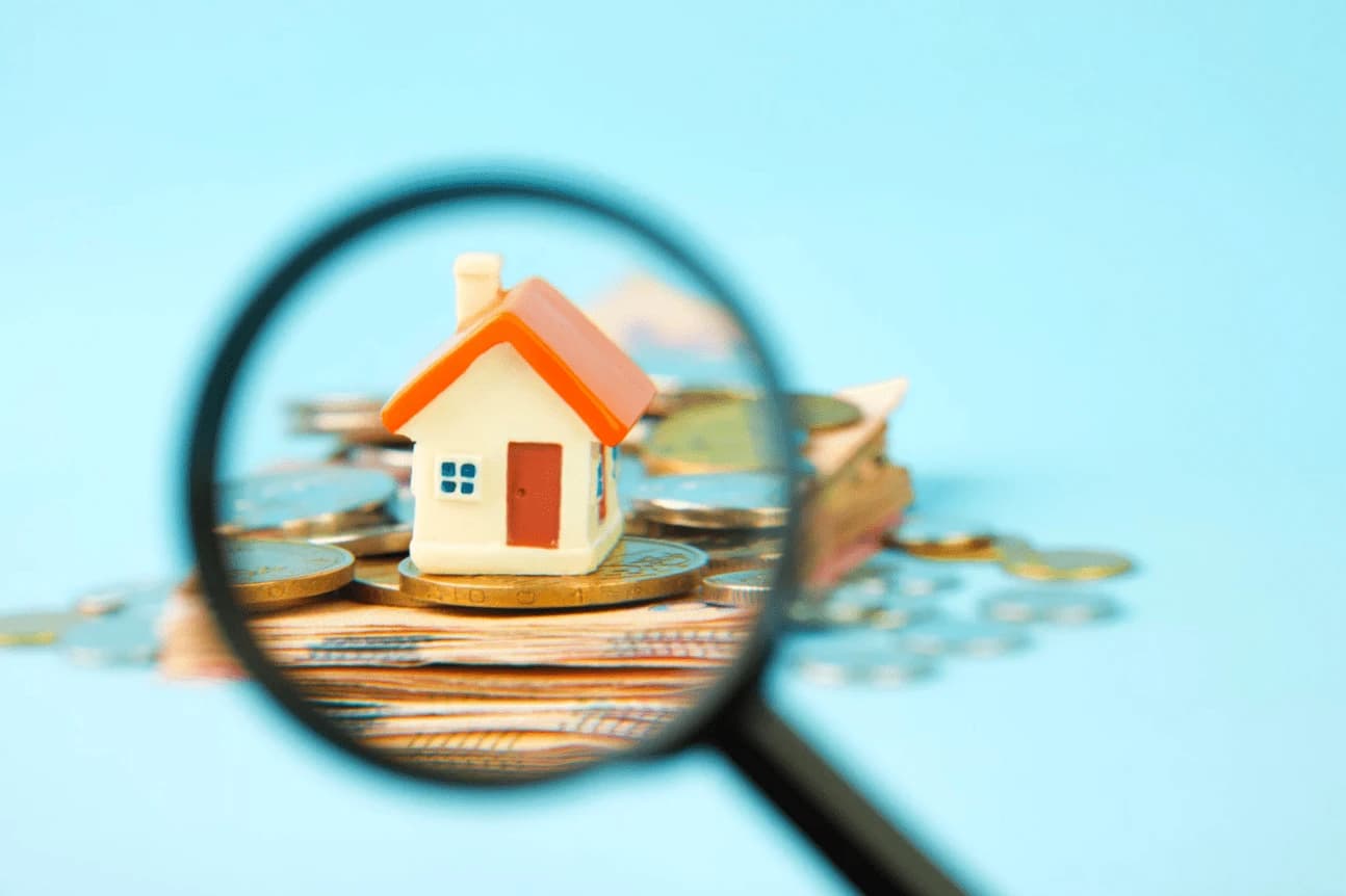 Miniature house on coins through magnifying glass